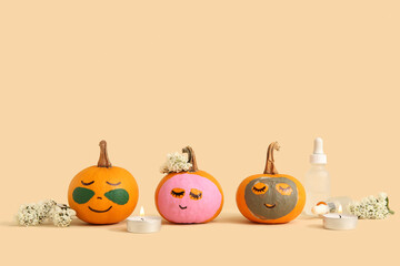 Pumpkins with masks, flowers, candles and cosmetic dropper bottles on beige background