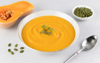 Pumpkin soup puree with creamy texture and pumpkin seeds on a gray background. 