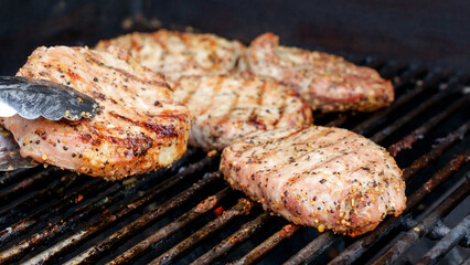 Grilled meat steak on stainless BBQ grill with flames on dark background. Food and cuisine concept.