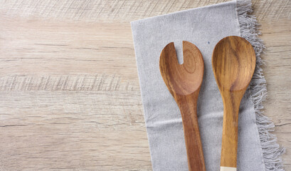 Two wooden spoons on a gray textile kitchen towel on a wooden background, top view