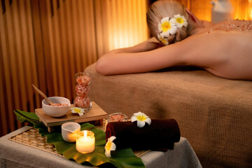 Obraz na płótnie Canvas Aromatherapy massage ambiance or spa salon composition setup with focus decor candles and spa accessories on blurred woman enjoying blissful aroma spa massage in resort or hotel background. Quiescent