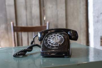 black old Traditional North American rotary dial telephone located on a metal table with a chair in...