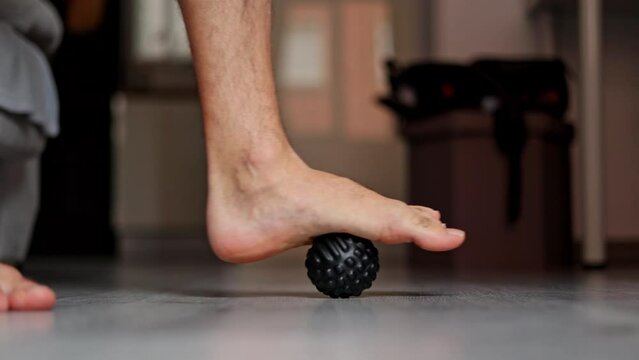 Close-up of the man foot steps on massage ball to relieve Plantar fasciitis or heel pain. A man massages his foot with a massage ball. Medical topics.