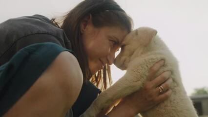 Pleased happy woman getting lovely puppy, playing and embracing four legged friend with love, standing in the garden. Humans and dogs. People lifestyle concept