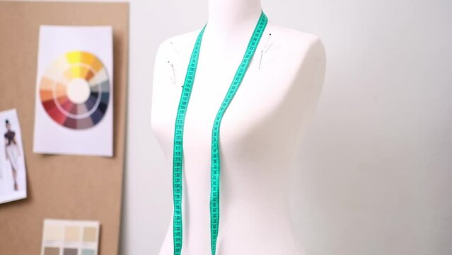 Green tape measure and pins on mannequin against board with swatches and sketches in fashion shop clothes sewing tools in contemporary atelier tailor studio closeup
