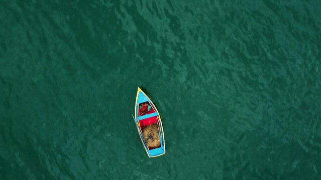 image from above of a red, blue and yellow fishing boat in a calm green ocean