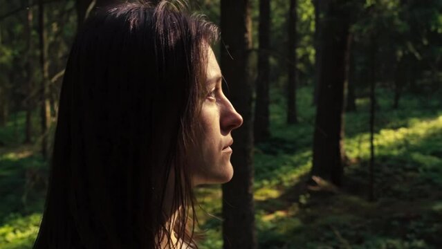 Young woman looks up through trees at sun in bavarian forest