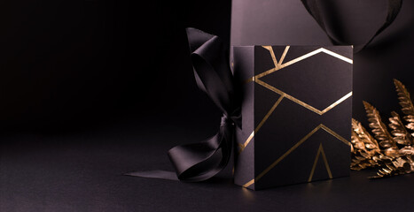 Black Friday Shopping Concept with Black color gift box decorated with Gold Stripes. Gift box Standing against shopping bag.