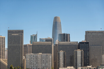 Fototapeta na wymiar San Francisco, CA, USA - July 13, 2023: Salesforce tower peeks above other skyscrapers in financial district under blue sky. Wall of concrete, glass and metal