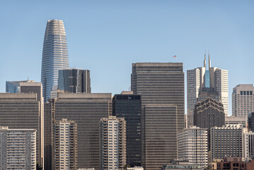 Fototapeta na wymiar San Francisco, CA, USA - July 13, 2023: Urban jungle of tall skyscrapers with Salesforce building peeking over the rest and California Center with its 2 sharp spires to the right, Light blue sky