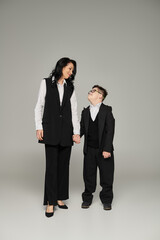 businesswoman and son with down syndrome holding hands, smiling at each other on grey, full length