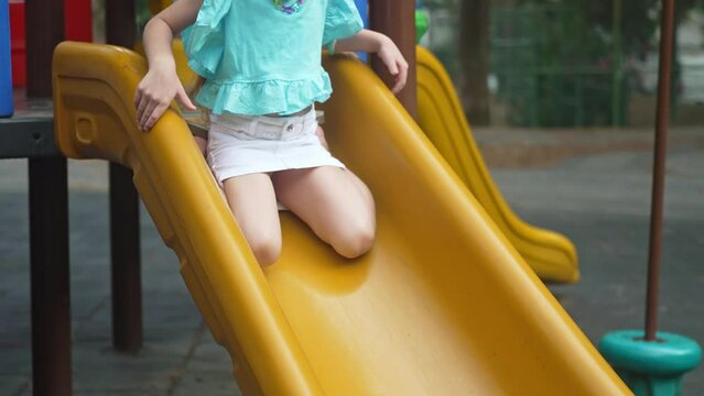 Little girl in stylish clothes rides yellow slide in maze on children playground happy schoolgirl plays attraction and runs in public park kid enjoys playtime