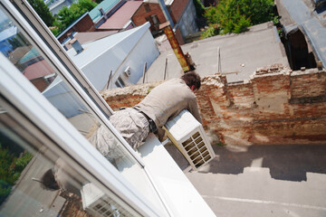without a face. A man installs an external air conditioner. dangerous work.