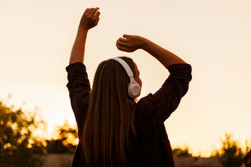 Silhouette of young woman in headphones enjoying music and dancing at sunset