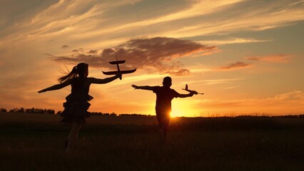 Children aviators boy girl run with toy plane across field in rays of sunset. Child wants to become...