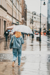Abstract silhouette of girl walking on rain under umbrella, street scene, back view. Seasons, weather, city lifestyle