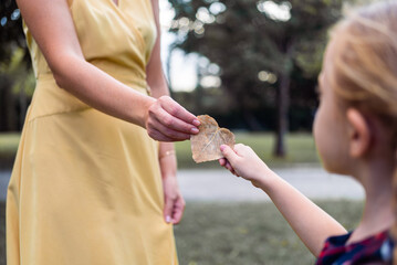 Woman and girl hold dry leaf in shape of heart closeup happy mother and little daughter rest together walking in park and demonstrating love on blurred background