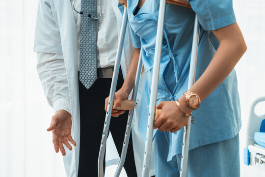 Doctor takes care of patient in crutch at hospital. Physical therapist and leg injury recovery concept. Jivy