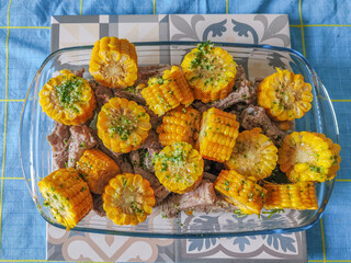 Cut cobs with pork chops and green Canarian mojo in a transparent bowl on a table with a blue tablecloth