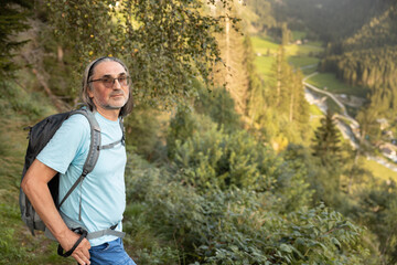 Portrait of man with backpack and sticks, descending from the mountain into the valley illuminated by the evening light