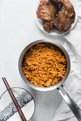 Jollof rice and fried chicken in a silver saucepan, homemade nigerian jollof rice in a pot, overhead view of authentic homemade west african jollof rice