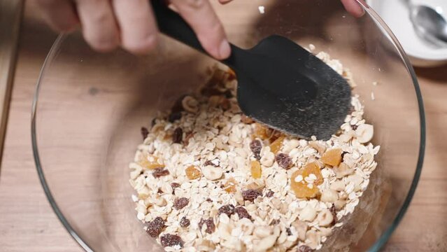 Ingredients for Granola, grains and a mixture of nuts and fruits, are being mixed together in a large bowl.