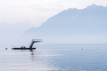Platform with a ladder and a springboard in a lake Leman, Switzerland with a Alps mountain landscape on a misty day.