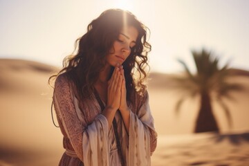 Expressive shot: a standing female aged 30 praying in the desert - obrazy, fototapety, plakaty