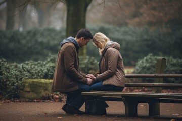 Emotive image of a standing couple aged 30 praying on a bench in a public park