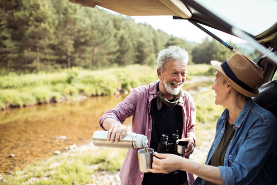 Senior couple drinking coffee in the morning while out camping or hiking in the forest by a creek
