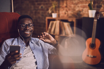 Young african american man listening to music on his smartphone on the couch in the living room