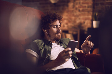 Young man using a smartphone while listening to music on the couch at home