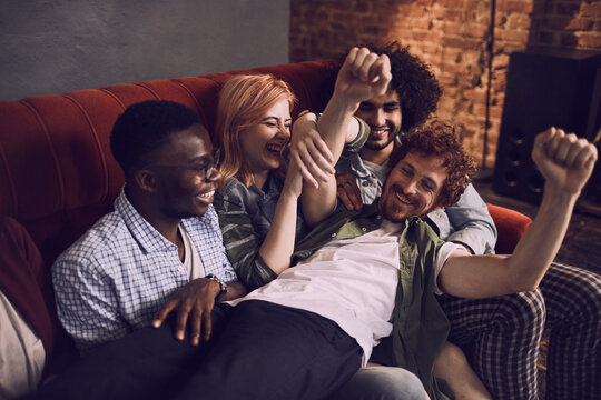 Young and diverse group of friends having fun and drinking beer on the couch at a house party