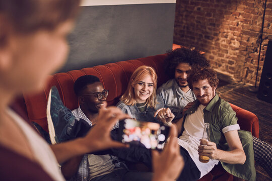Young and diverse group of friends taking a picture with a smartphone while having fun and drinking beer on the couch