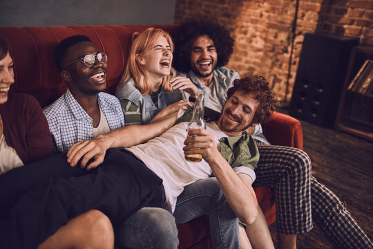 Young and diverse group of friends having fun and drinking beer on the couch at a house party