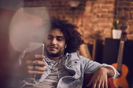 Young man using a smartphone while listening to music on the couch at home