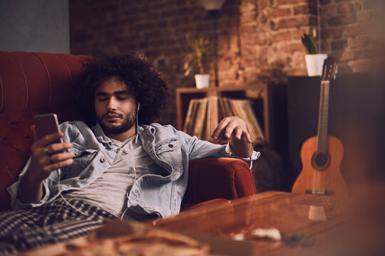 Young man using a smartphone while listening to music on the couch at home
