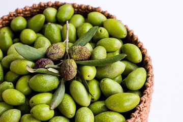 Freshly harvested green natural olives in wicker basket on white surface