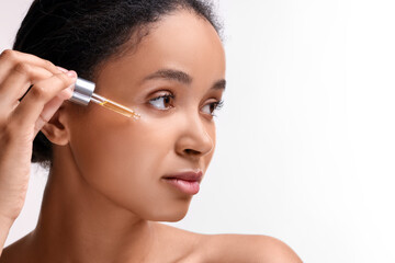 Beautiful woman applying serum onto her face on white background, closeup. Space for text