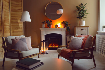 Stylish fireplace near comfortable armchairs and coffee table in cosy living room. Interior design
