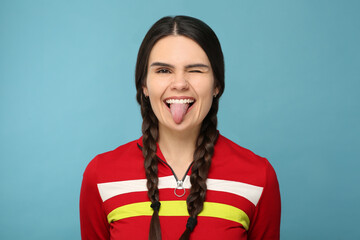 Happy young woman showing her tongue on light blue background