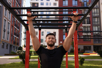 Smiling man training on monkey bars at outdoor gym