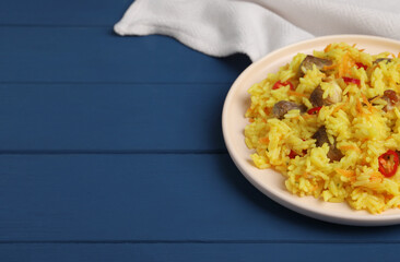 Delicious pilaf with meat on blue wooden table. Space for text