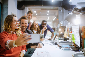 Diverse group of coworkers taking a selfie on a smartphone in the office of a startup company