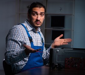 Young male technician repairing computer in workshop at night