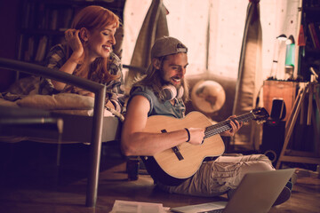 Young couple playing the guitar and singing together in the bedroom at home