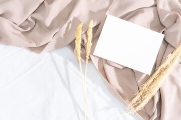 Minimalist square invitation card mockup on wavy white fabric with dried plants and window shadow background
