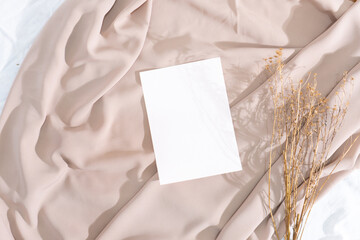 Minimalist square invitation card mockup on wavy white fabric with dried plants and window shadow background
