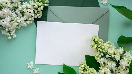 Composition with empty green envelope and beautiful spring lilac flowers on mint background. Mockup card invitation greeting card postcard copy space template blank. Branches of lilac blooming bouquet