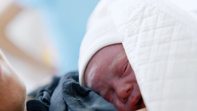 Little red crying newborn lying on his mom's chest. Just born baby covered in blankets. Close up portrait.